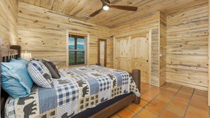 Ein Schlafzimmer einer Holzhütte mit Bett, Deckenventilator und Fenster mit Jalousien.