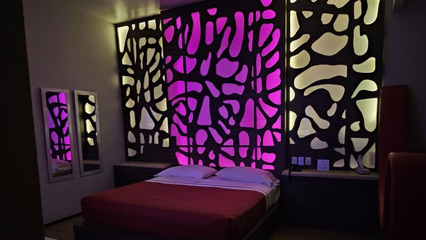 A bedroom with a bed, a nightstand, a chair, and a decorative wall panel. - ROYAL BOUTIQUE (Torreón)