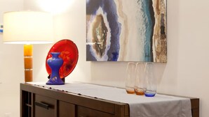 A room with a wooden cabinet, a table with a white cloth, a blue vase, a red glass object, and a painting on the wall. - Stylish Spacious Greentree Apartment (Bethesda)