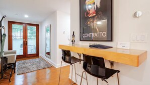 A modern interior with a wooden desk, two black bar stools, a framed artwork, and a glass door leading to an outdoor area. - Stylish Spacious Greentree Apartment (Bethesda)