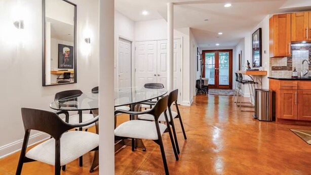 A modern kitchen with wooden cabinets, a stainless steel sink, and a dining area with a glass table and chairs. - Stylish Spacious Greentree Apartment (Bethesda)