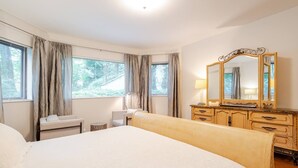 A bedroom with a large bed, a dresser with a mirror, a bedside table, and curtains on the windows. - Stylish Spacious Greentree Apartment (Bethesda)