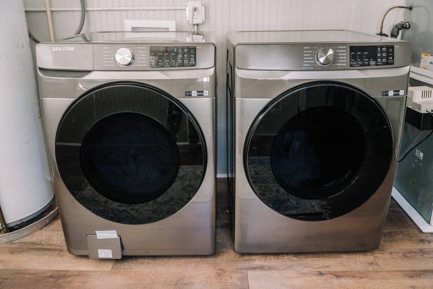 Two front-loading washing machines with control panels, placed side by side on a wooden floor.