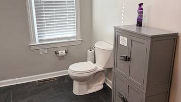 Ein Badezimmer mit Toilette, einem Schrank, einem Fenster mit Jalousien und einem gerahmten Bild an der Wand.