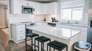 Una cocina moderna con armarios blancos, una isla grande con taburetes de bar, un microondas integrado y una cafetera.