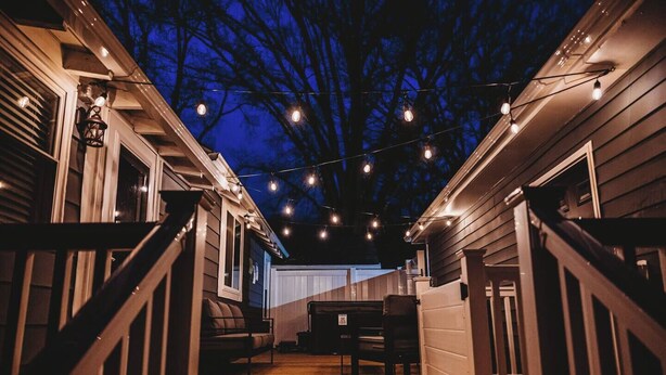 Una terraza de madera con luces colgantes, un banco y una mesa.