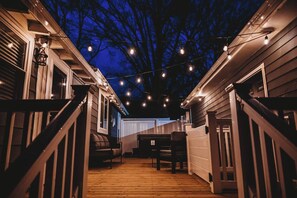 Una terraza de madera con luces colgantes, un banco y una mesa.
