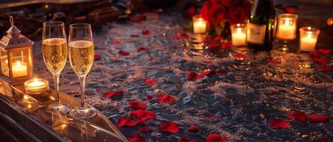 Escena romántica con una mesa dispuesta para dos personas, con copas de champán, velas y pétalos de rosa.