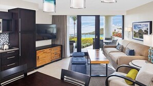 A modern living room with a sofa, coffee table, and TV. There is a kitchen area with cabinets and a TV. The room has large windows with a view of the outdoors. - Luxury 2 BR Coral Vista Villa - Westin St John (Cruz Bay)