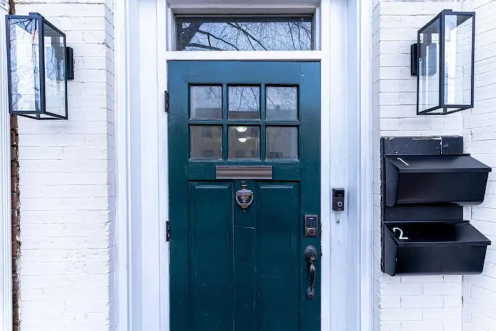 A green door with a window, a mailbox, and two wall-mounted lanterns.