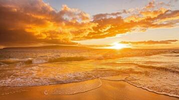 A beach with waves, a sunset, and a clear sky.