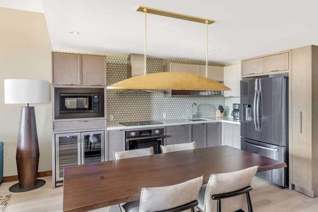 A modern kitchen with a dining table, stainless steel appliances, and a pendant light.