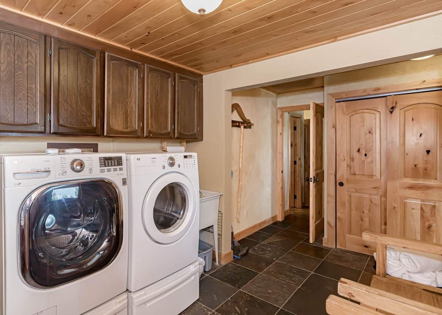 A laundry area with two front-loading washing machines, wooden cabinets, and a wooden door.