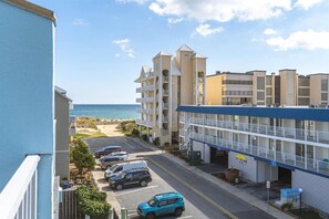 A beachfront hotel with multiple balconies, a parking lot, and a view of the ocean.