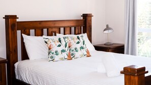 A neatly made bed with a floral pillow, a wooden headboard, and a bedside table with a lamp.
