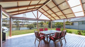 Un porche cubierto al aire libre con una mesa, sillas, una parrilla y vistas a un lago y follaje circundante.