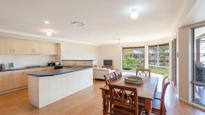 A modern kitchen with wooden cabinets, a dining area with a table and chairs, and a large window offering a view of the outdoors.