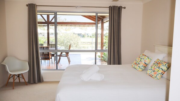 A bedroom with a large bed, a chair, and a view of an outdoor deck.