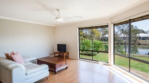 A spacious living room with a large window, a ceiling fan, and a flat-screen TV on a wooden stand.
