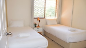 Una habitación de hotel con dos camas, una mesita de noche, una lámpara y una ventana con persianas.