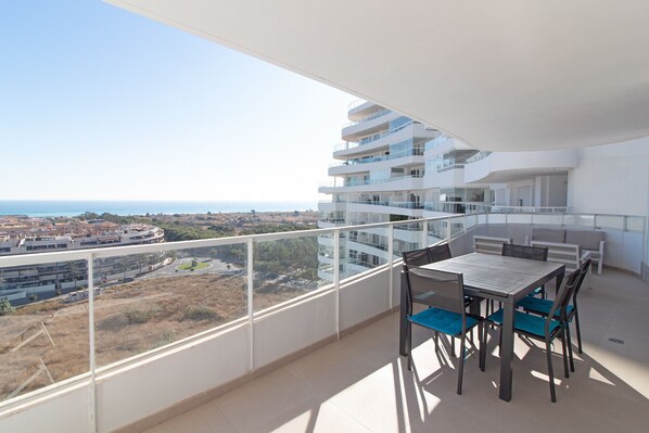 A balcony with a table and chairs, overlooking a coastal area with buildings and a view of the sea. - Global Vacacional: Modern flat with two terraces with sea and mountain views (Canet d´en berenguer)
