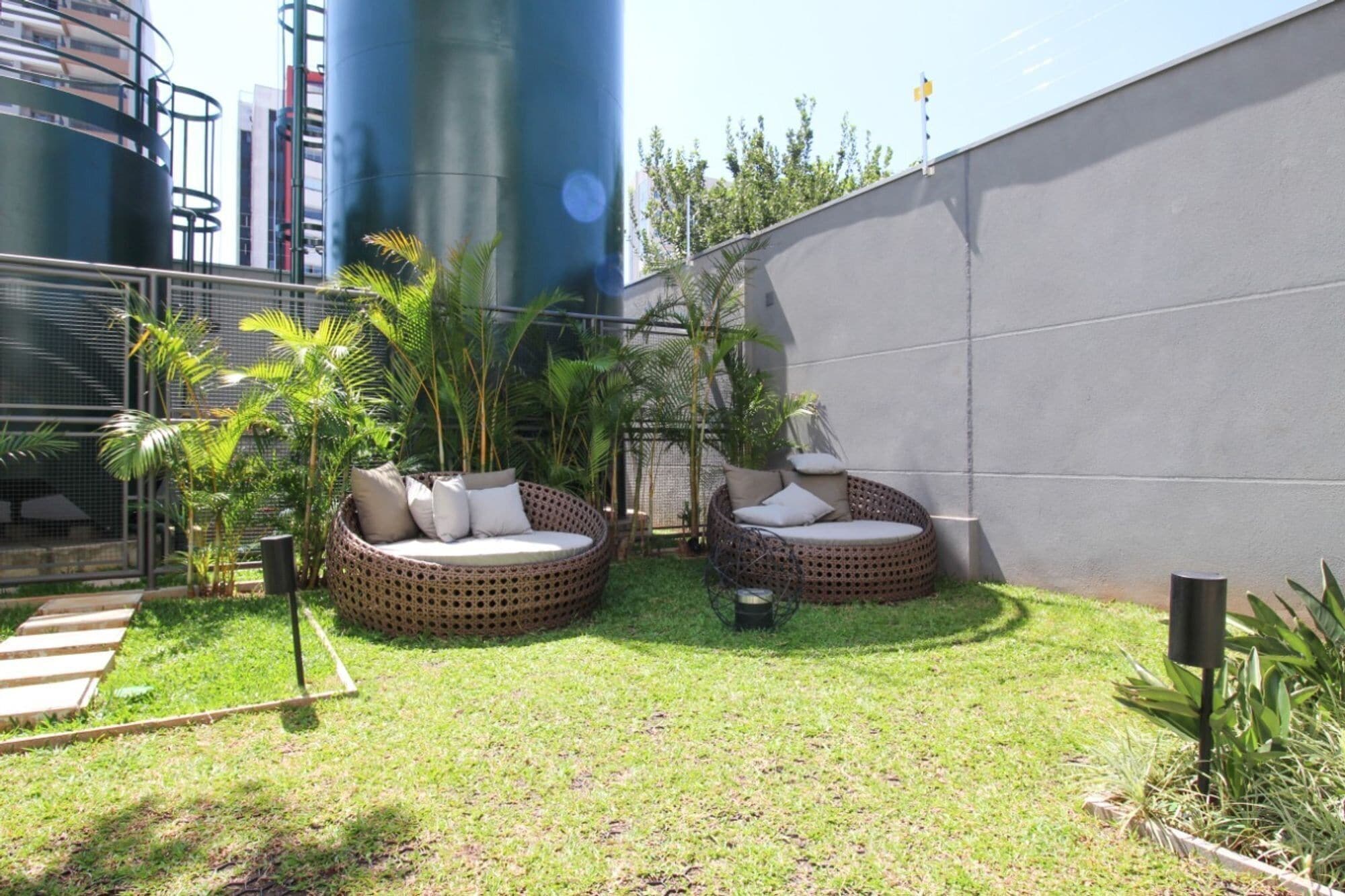 A courtyard with two wicker chairs and a small table, surrounded by grass and plants.