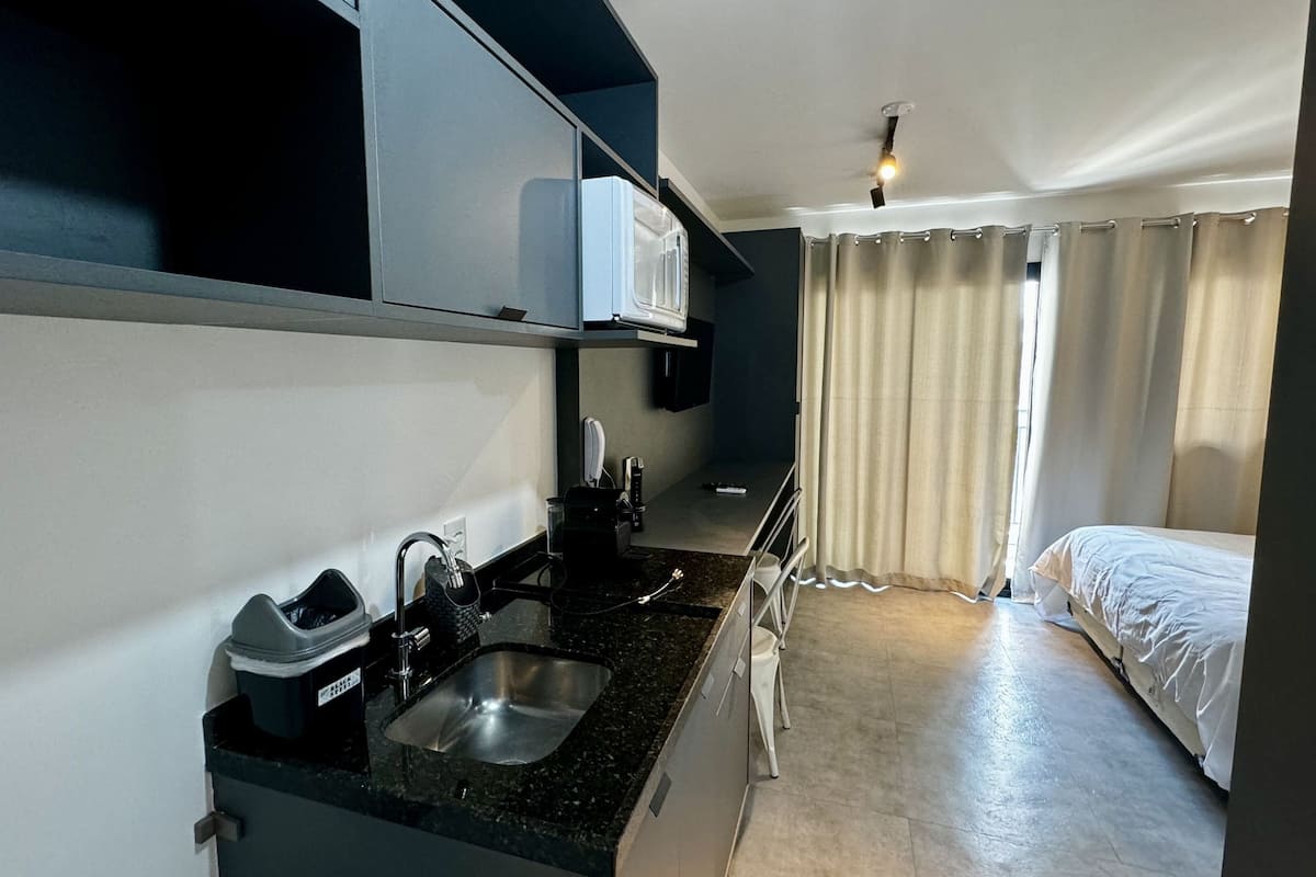 A compact hotel room with a kitchenette, a bed, and a window with curtains.