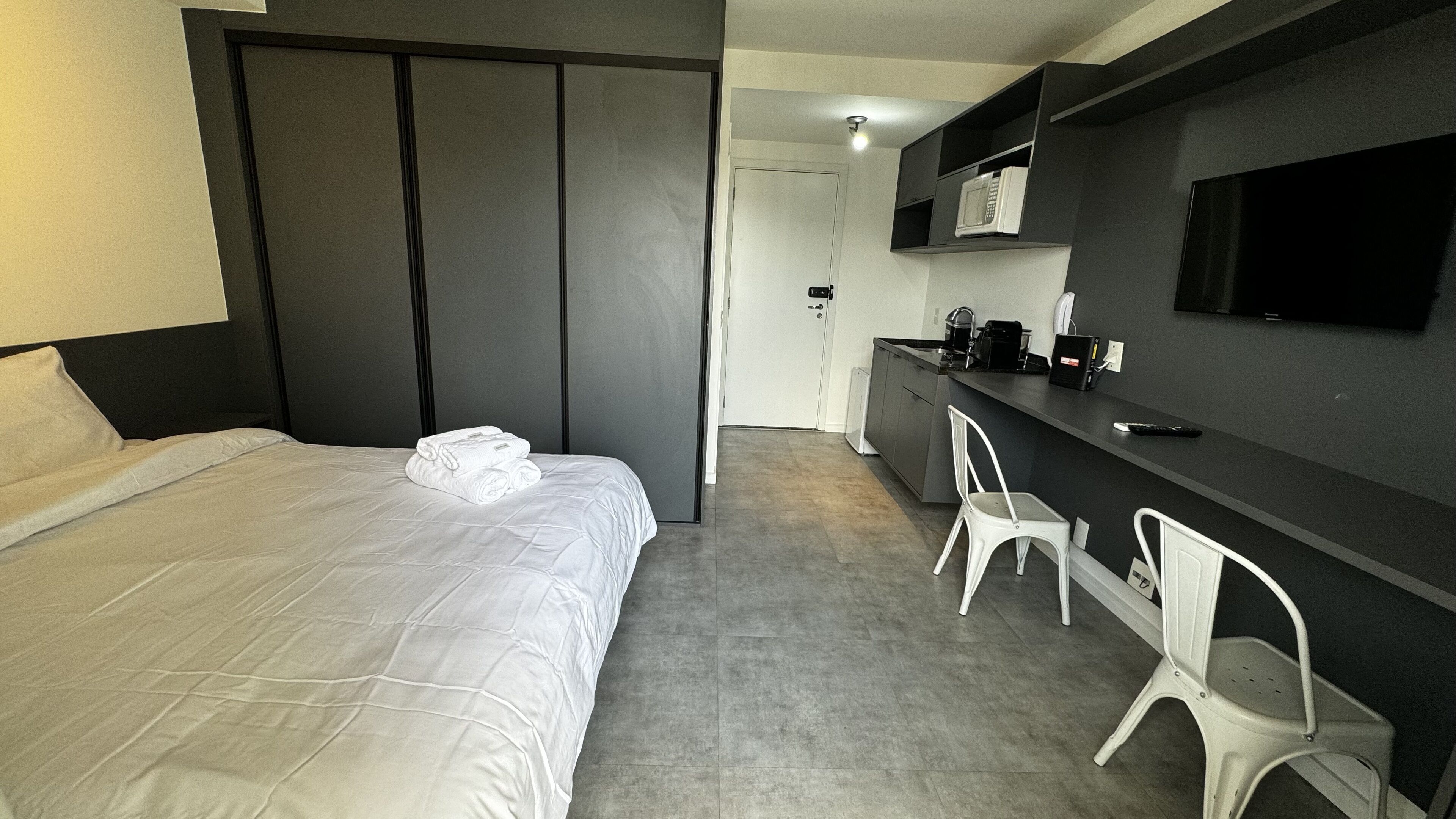 A hotel room with a bed, a desk, a chair, a microwave, and a TV.