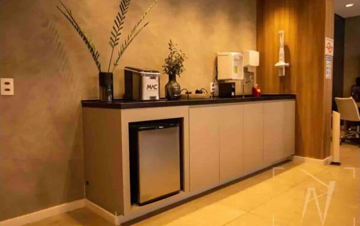 A reception desk with a built-in refrigerator, a vase with a plant, and a MAC box.