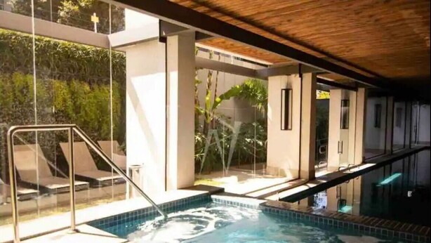 Une piscine intérieure moderne avec des parois en verre transparent, un plafond en bois et une vue sur la verdure environnante.