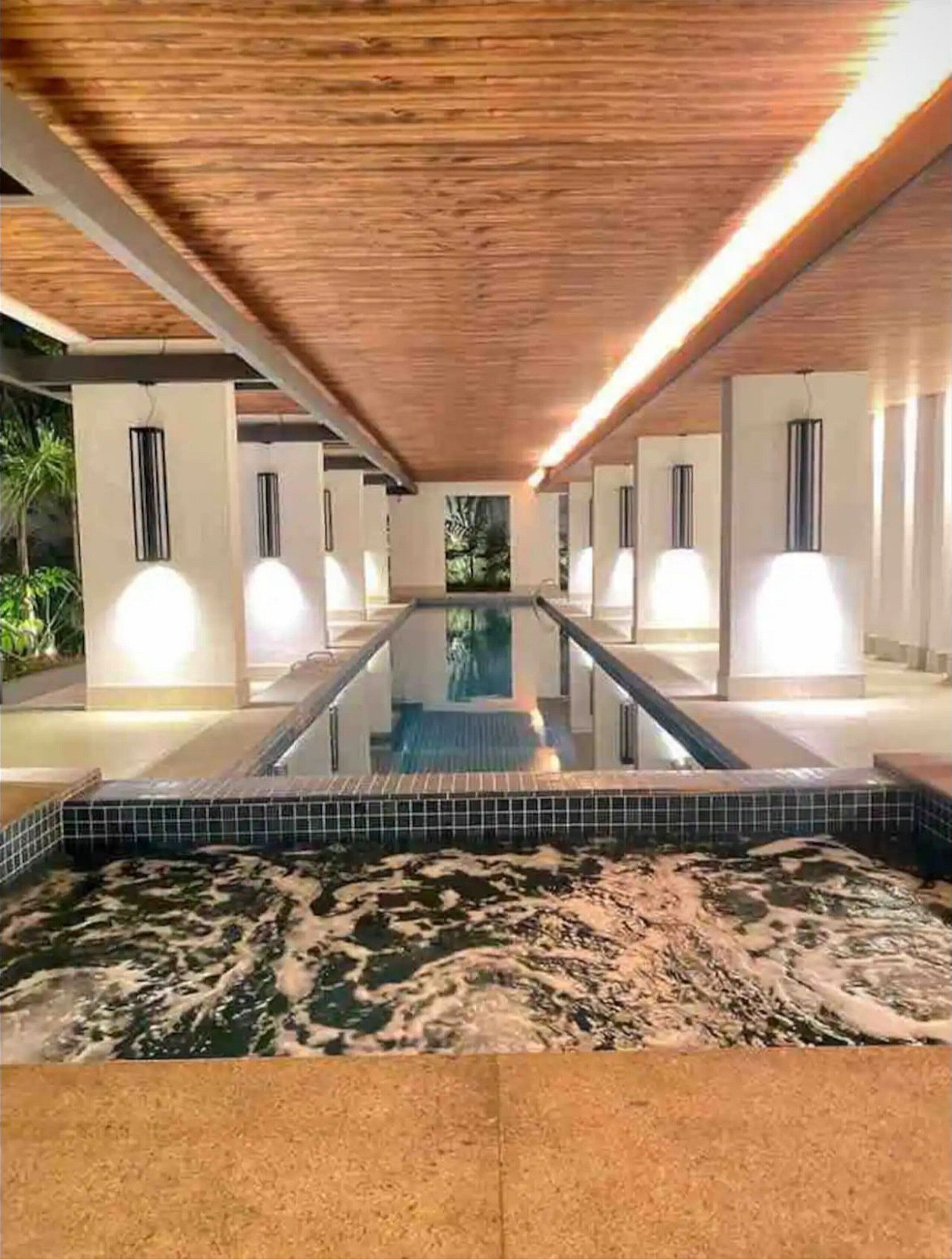 A long, narrow indoor swimming pool with a tiled floor, surrounded by columns and recessed lighting.