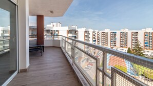 Un balcon doté d’un plancher en bois, d’une rambarde en métal et offrant une vue sur des immeubles de grande hauteur.