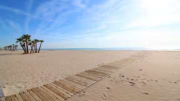 Een zandstrand met een houten promenade en palmbomen.