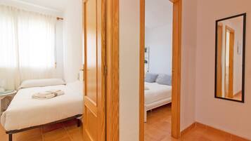 Een hotelkamer met een bed, een nachtkastje, een spiegel en een deur die naar een andere kamer leidt.