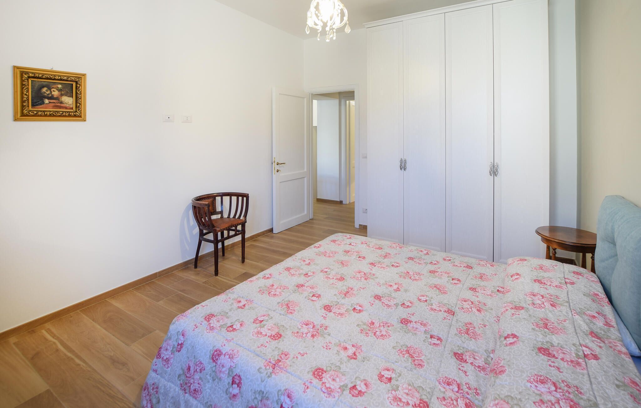 Une chambre à coucher avec une couvre-lit à motifs floraux, une chaise en bois, une armoire et un lustre.