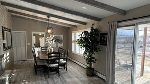 A dining area with a wooden table, chairs, and a hanging light fixture. There is a potted plant and a painting on the wall. - Located on a beautiful ranch! Relax with mountain view’s & a pool table (Cody)