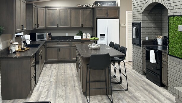 A modern kitchen with dark wood cabinets, a central island, and a brick accent wall. - Located on a beautiful ranch! Relax with mountain view’s & a pool table (Cody)