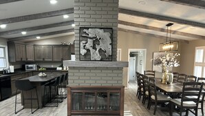 A modern kitchen with a central island, dark wooden cabinets, and a large fireplace with a rustic design. - Located on a beautiful ranch! Relax with mountain view’s & a pool table (Cody)