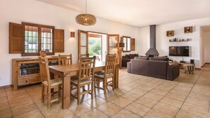 A spacious living area with a dining table, chairs, a sofa, a TV, and a fireplace. - Villa Dalt S Era with Mountain View, Wi-Fi, Air Conditioning, Pool & Garden (Santa Gertrudis de Fruitera)