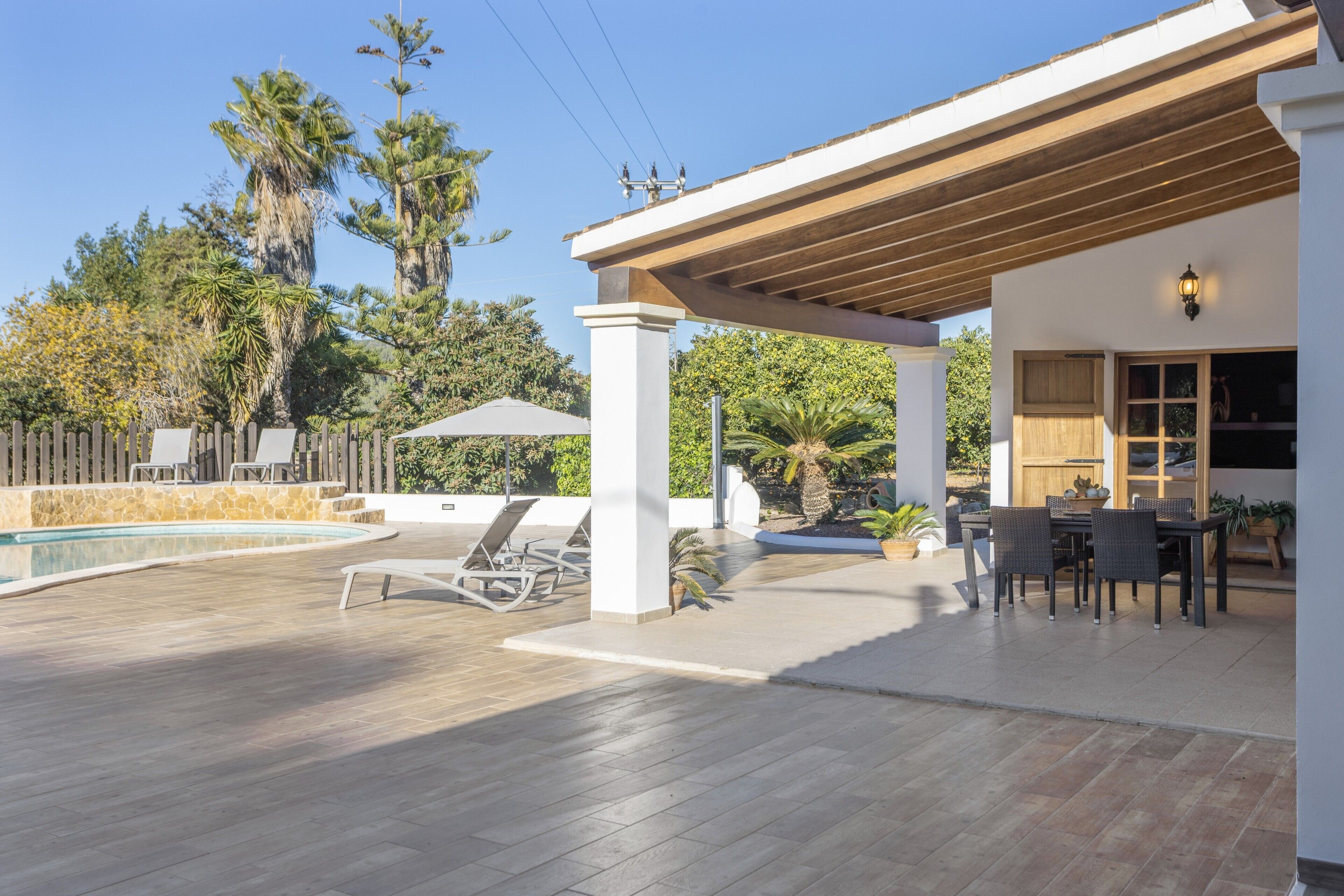 En overdækket udendørs terrasse med pool, liggestole og spiseplads.
