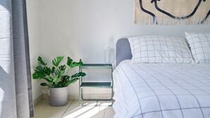 Ein ordentlich eingerichtetes Schlafzimmer mit einem Bett, einem Nachttisch, einer Zimmerpflanze und einem Wandbild.
