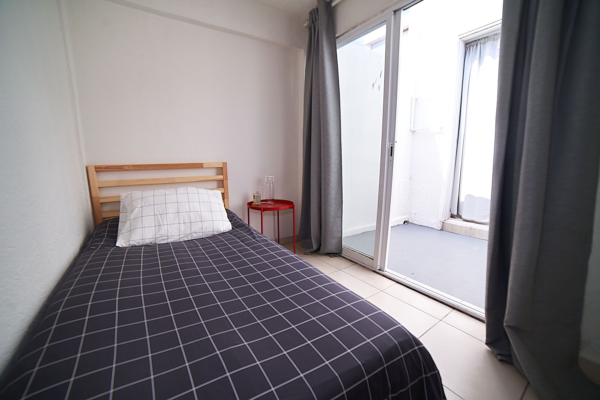 A bedroom with a bed, a small table, and a sliding glass door leading to an outdoor area.
