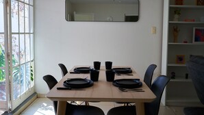 Ein Essbereich mit einem Tisch für sechs Personen, Stühlen, einem Wandspiegel und einer Bücherwand mit diversen Gegenständen.