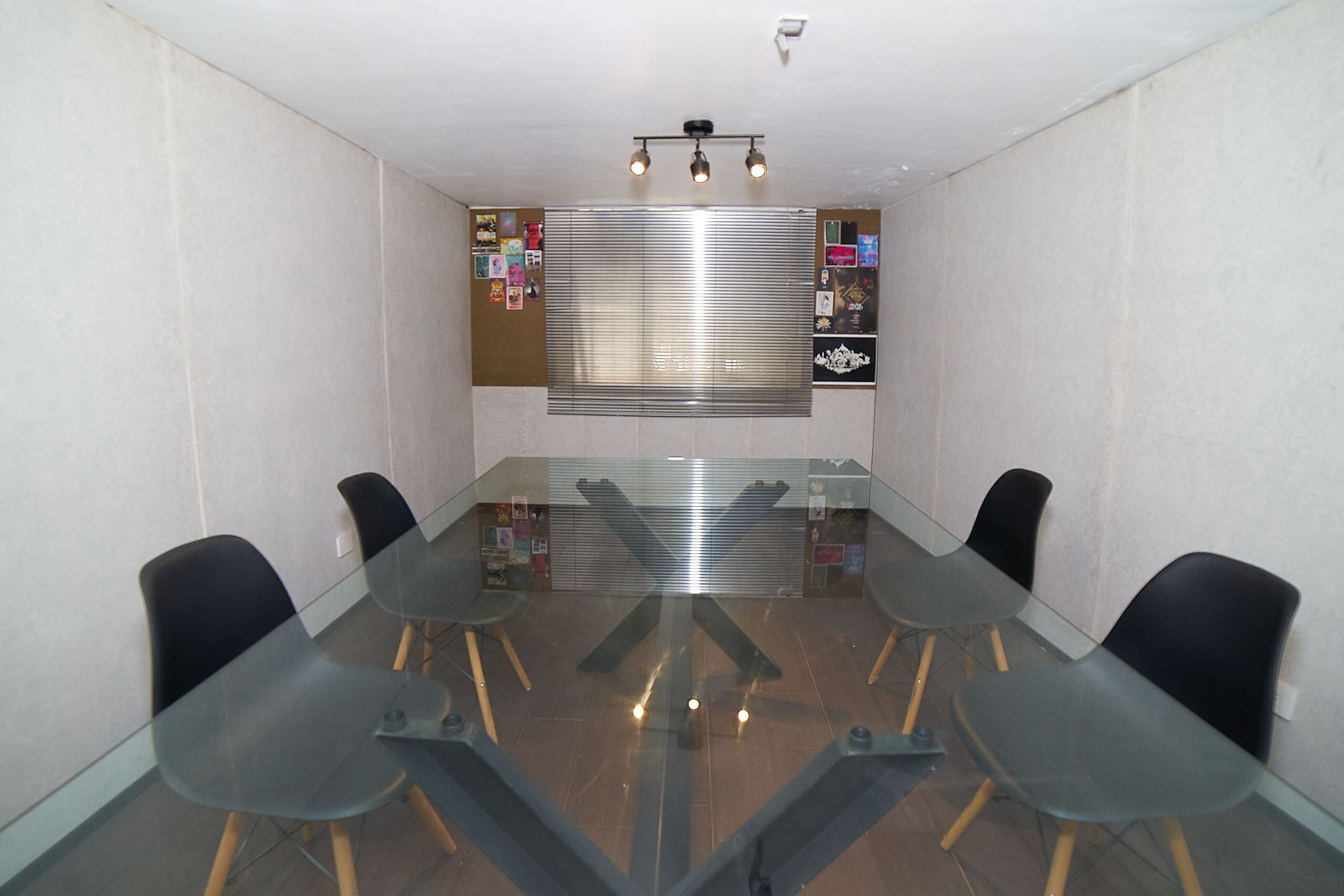 Een vergaderruimte met een glazen tafel, zwarte stoelen en een prikbord met diverse berichten.