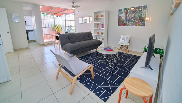 Ein modernes Wohnzimmer mit einer Couch, einem Couchtisch und einem Fernseher. Ein Bücherregal und ein Gemälde sind an der Wand zu sehen.