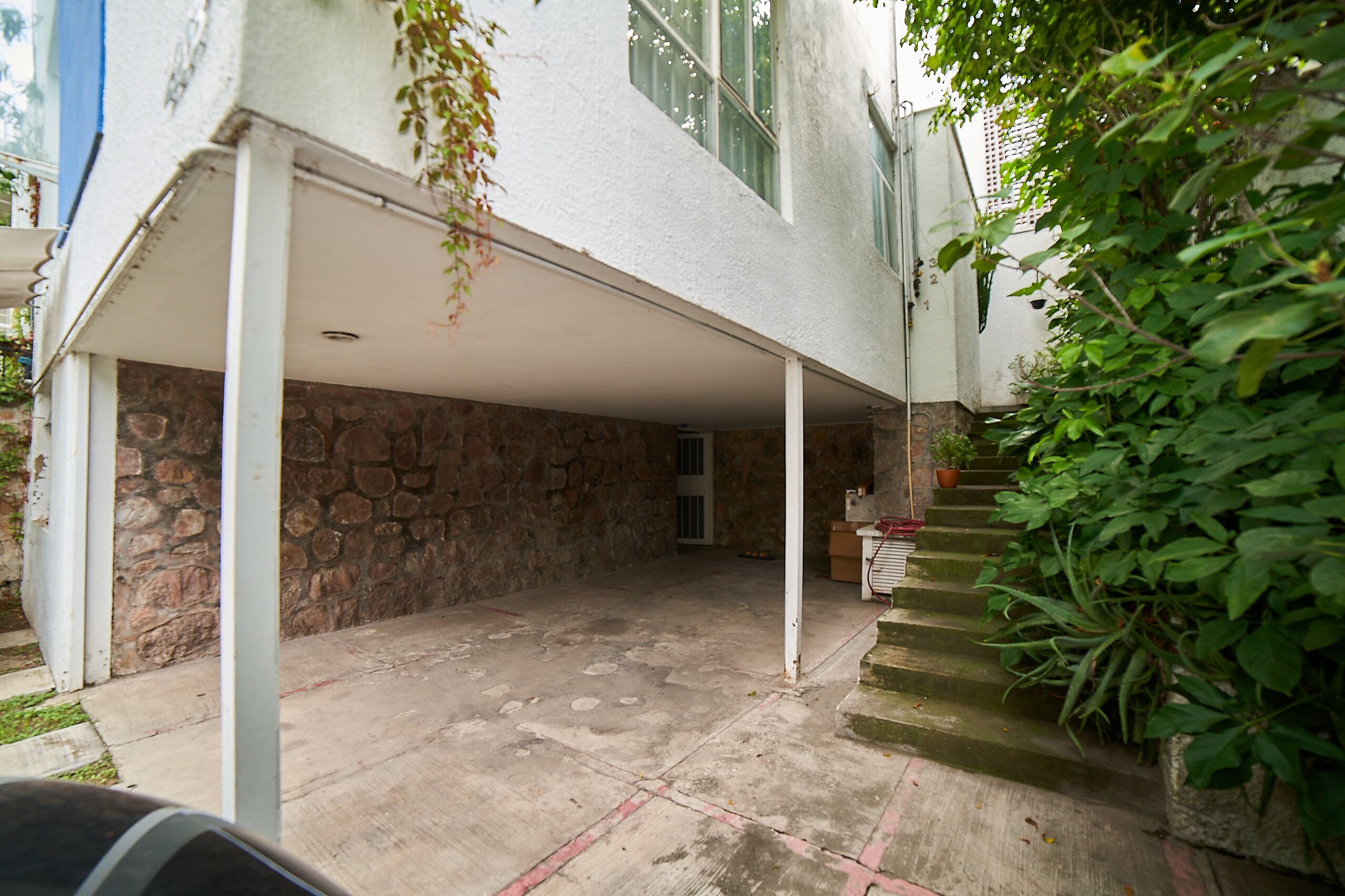 Un espace extérieur abrité, doté de murs en pierre, d’un sol en béton et d’un escalier menant à une porte.