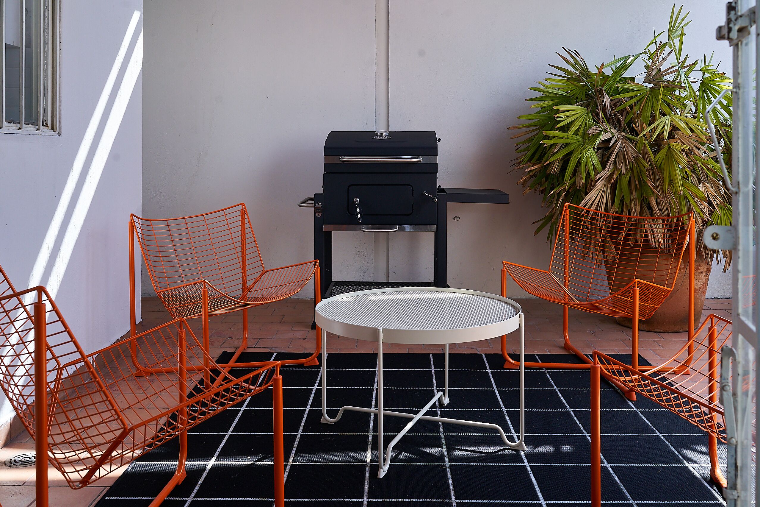 Een klein buitgedeelte met een barbecue, stoelen en een potplant.