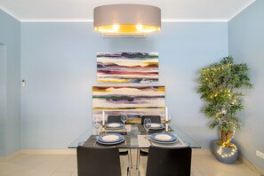 Comedor con una mesa preparada para dos personas, un cuadro abstracto moderno y una planta decorativa con luces.