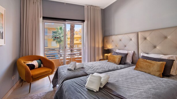 Een hotelkamer met twee bedden, een slaapbank, uitzicht op gebouwen en een balkon.