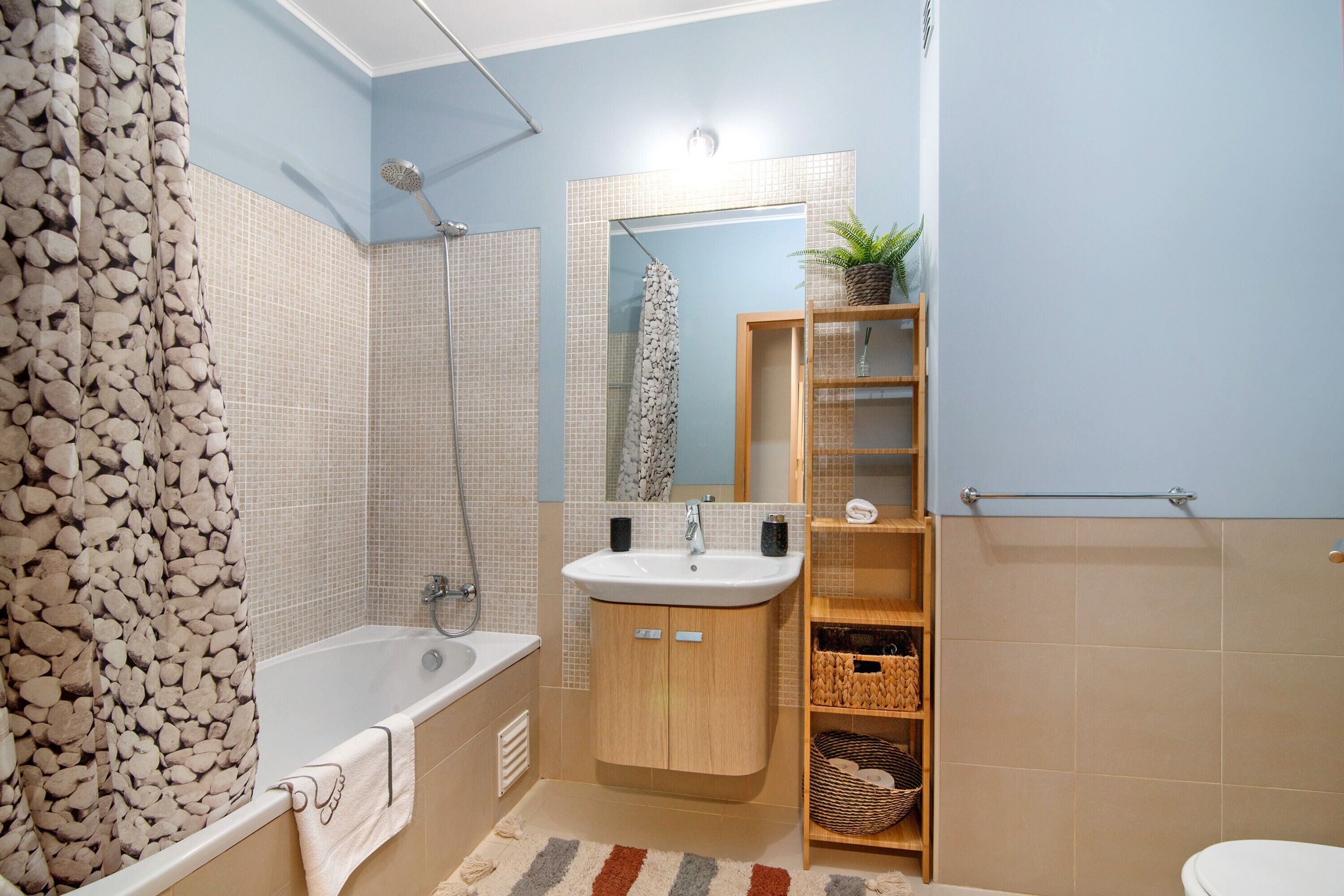 Un baño con bañera, lavabo, ducha y estante de madera con cestas.